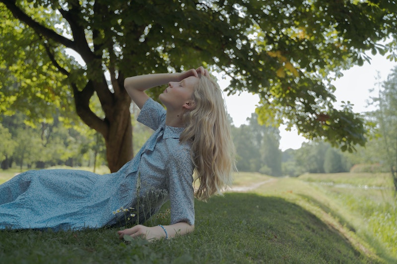Eine junge Frau mit blonden Haaren trägt ein hellblaues Sommerkleid und liegt im Gras
